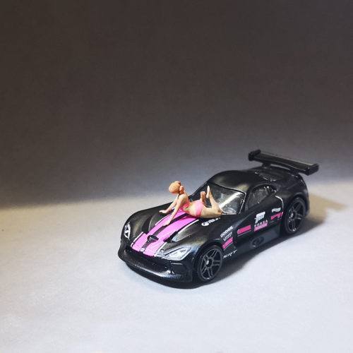 1-64 scale slender girl lay down on the car. A slender girl with two ponytails in a bikini playfully lies on the roof of a car.