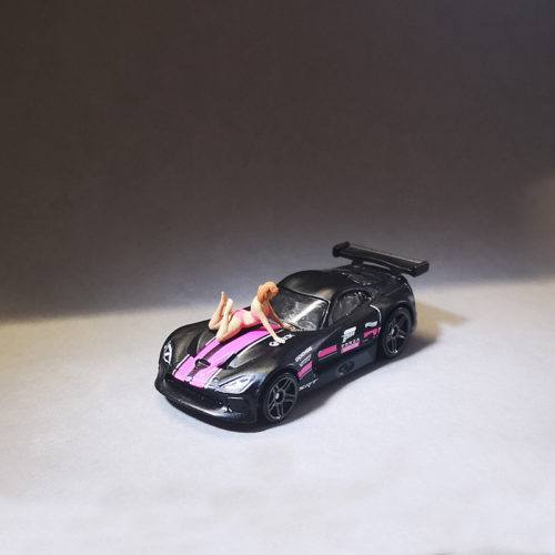 1-64 scale slender girl lay down on the car. A slender girl with two ponytails in a bikini playfully lies on the roof of a car.